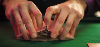 Mãos a baralhar um baralho de cartas sobre uma mesa de pano verde num jogo de Gin Rummy