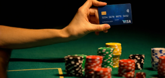 Mão a segurar cartão Visa sobre mesa de casino com fichas