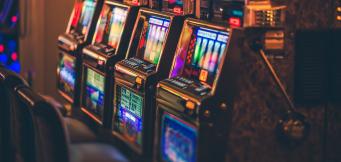 Fila de slot machines iluminadas por néon numa sala de casino, representando as slots que mais pagam num ambiente de jogo ao vivo