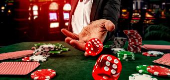 Jogador de casino de fato lança dados vermelhos sobre mesa verde com fichas e cartas