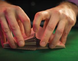 Mãos a baralhar um baralho de cartas sobre uma mesa de pano verde num jogo de Gin Rummy