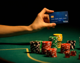 Mão a segurar cartão Visa sobre mesa de casino com fichas