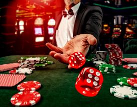 Jogador de casino de fato lança dados vermelhos sobre mesa verde com fichas e cartas