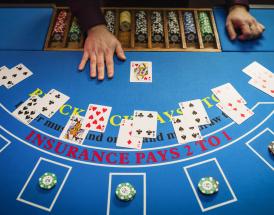 Mesa de blackjack vista de cima com cartas distribuídas, fichas de casino e mão do dealer durante uma ronda