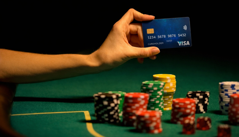 Mão a segurar cartão Visa sobre mesa de casino com fichas