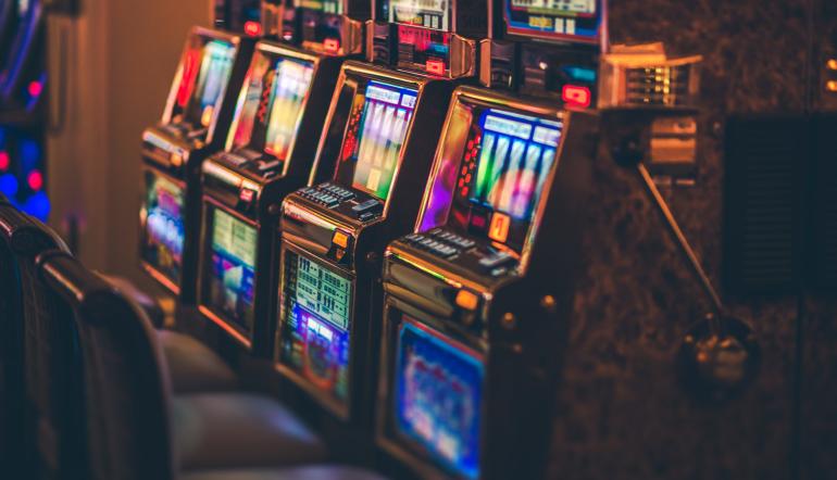 Fila de slot machines iluminadas por néon numa sala de casino, representando as slots que mais pagam num ambiente de jogo ao vivo