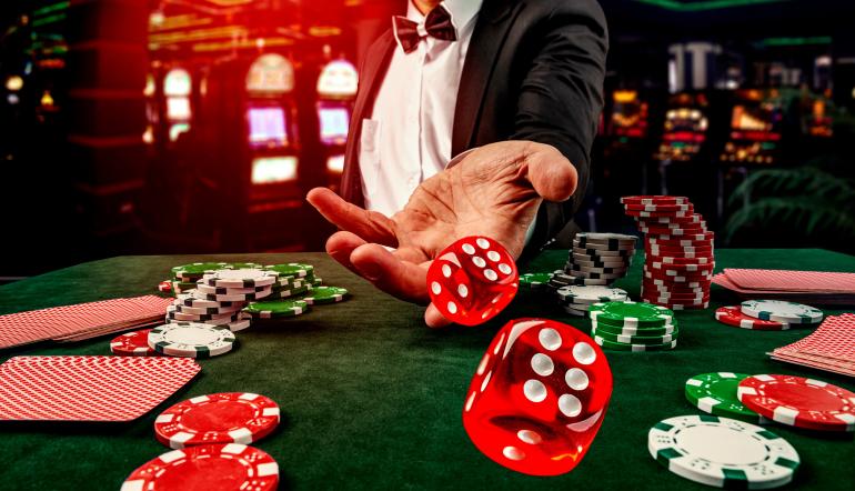Jogador de casino de fato lança dados vermelhos sobre mesa verde com fichas e cartas