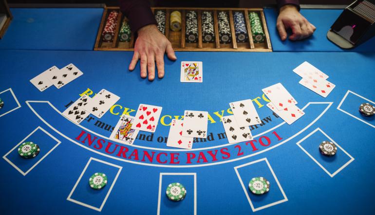 Mesa de blackjack vista de cima com cartas distribuídas, fichas de casino e mão do dealer durante uma ronda