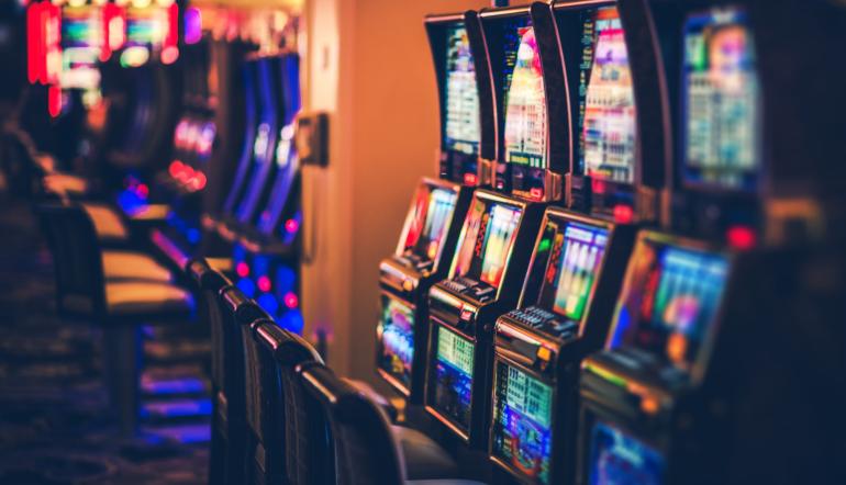 Fila de slot machines num casino com iluminação ambiente e luzes neon desfocadas ao fundo