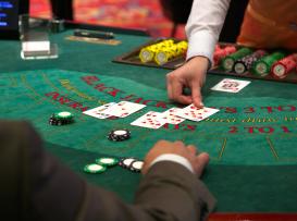 Dealer a revelar cartas numa mesa de blackjack com fichas do jogador apostadas