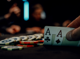 Jogador segura dois ases com fichas de poker empilhadas em mesa de casino escura