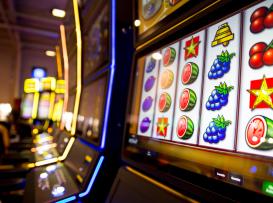 slot machines num casino, com símbolos de frutas nos cilindros e luzes néon ao fundo