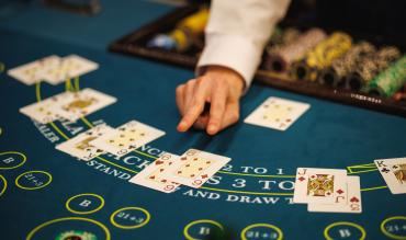 Dealer a distribuir cartas numa mesa de blackjack com fichas e várias mãos em jogo