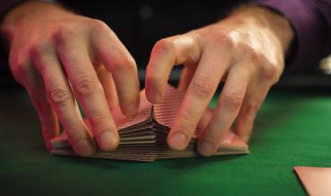 Mãos a baralhar um baralho de cartas sobre uma mesa de pano verde num jogo de Gin Rummy