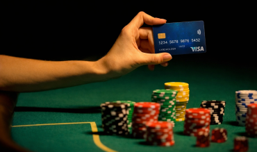Mão a segurar cartão Visa sobre mesa de casino com fichas