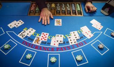 Mesa de blackjack vista de cima com cartas distribuídas, fichas de casino e mão do dealer durante uma ronda