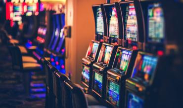 Fila de slot machines num casino com iluminação ambiente e luzes neon desfocadas ao fundo